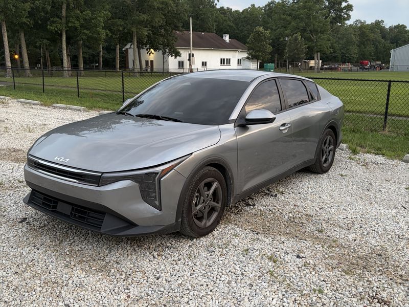 Car window tint in Charlotte, NC: Gray Kia K4 sedan with dark tinted windows parked on gravel