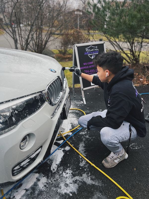 Mobile hand car wash in Charlotte, NC: Detailer brushing foam out of the grille of a white BMW X3