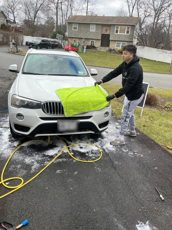 Premium mobile car detailing in Raleigh, NC: Detailer drying the hood of a white BMW X3 with a large microfiber drying towel