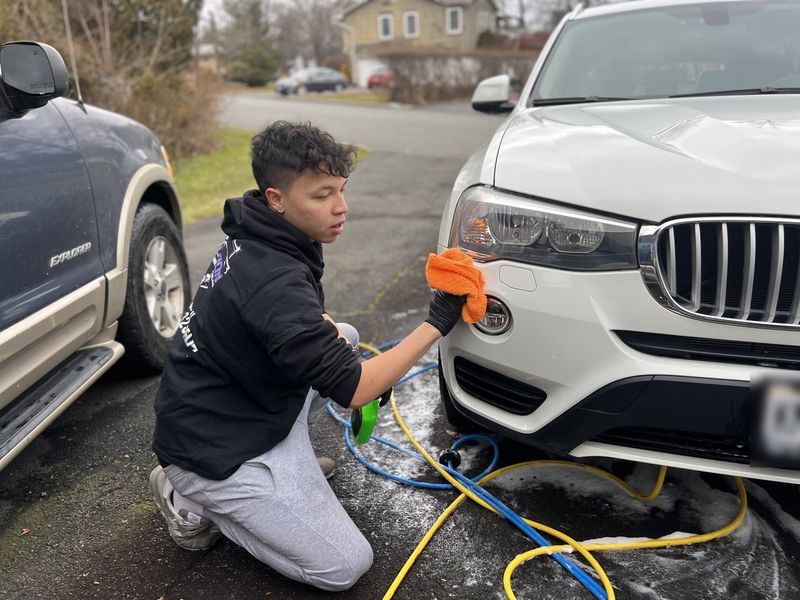 Mobile exterior detailing in Charlotte, NC: Detailer wiping the front bumper and fog light of a white BMW X3