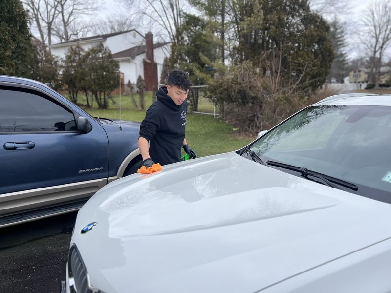 Mobile exterior detailing in Charlotte, NC: Detailer wiping down the hood of a white BMW X3 next to the Motion truck