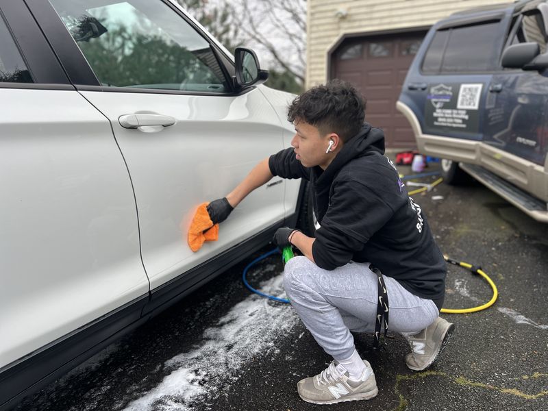 Mobile car detailing in Charlotte, NC: Motion Mobile Detailing detailer wiping down a white BMW X3 in a customer driveway, with the Motion truck behind him