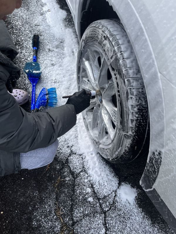 Mobile hand car wash in Charlotte, NC: Wheel covered in foam being cleaned with a detailing brush, wheel brushes on the ground